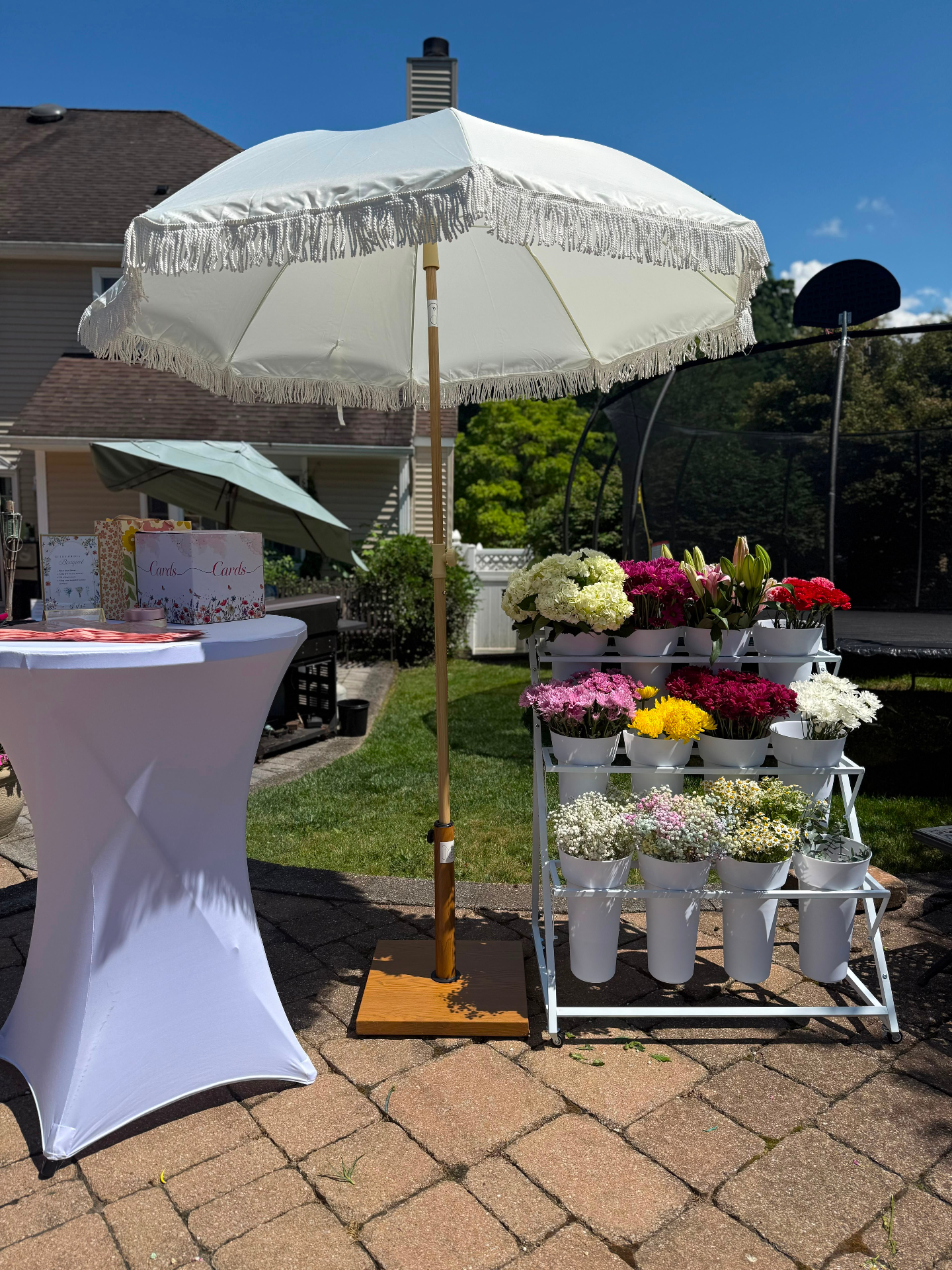 Outdoor bloom bar setup with fringe umbrella and cocktail table in Bergen County, NJ
